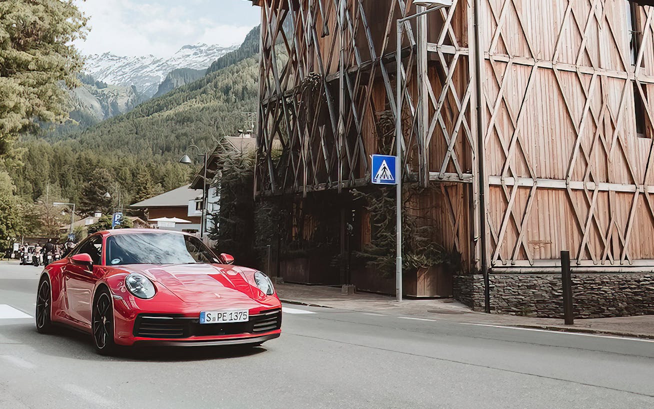 Red Porsche 911 drives past house with wood panelling