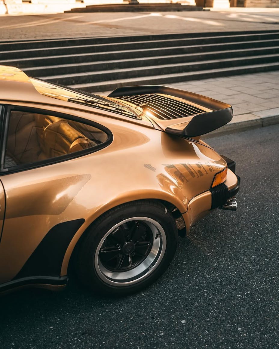 Rear view of a gold classic Porsche 911 parked beside steps in the city