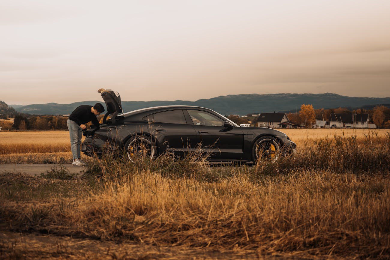 Man leaning into Porsche Taycan boot while parked in field