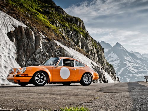 Orange classic Porsche on Swiss Alpine road, mountains in background