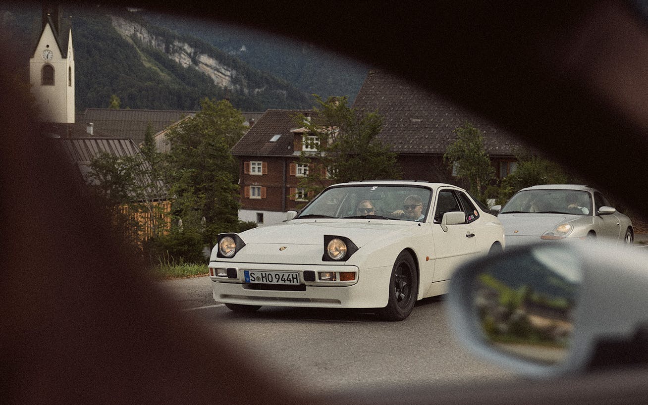 White Porsche 944 drives through Alpine village road