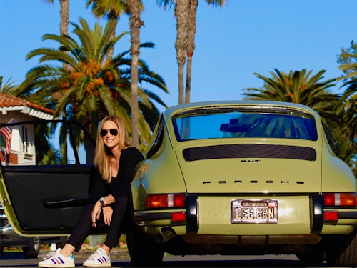 Woman sits in green Porsche 911 with palm trees behind
