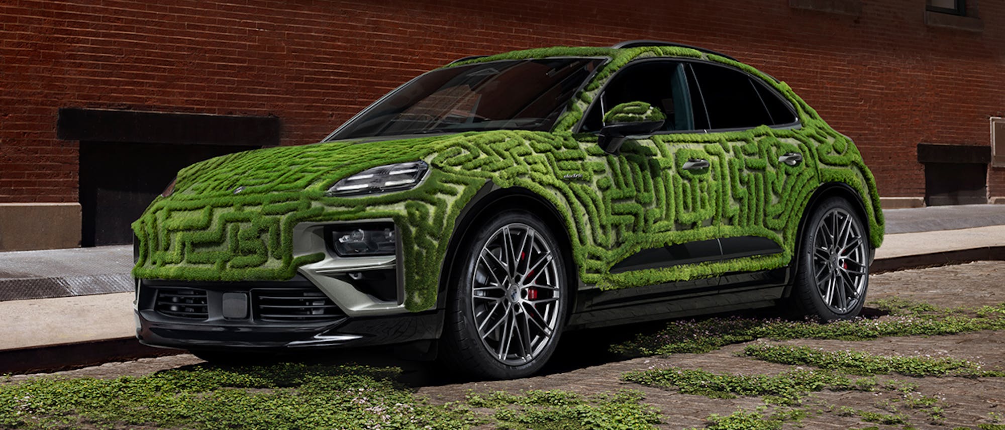 Porsche Macan covered in green moss, in front of brick building