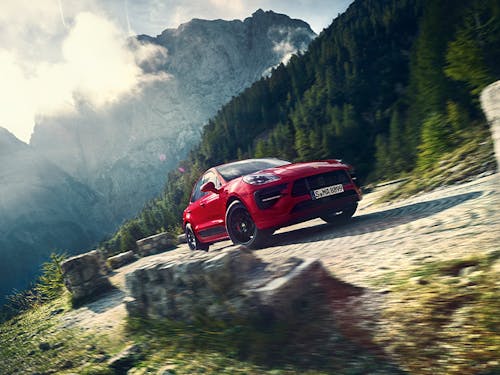 Red Macan GTS on cobbled road, cloudy sunlit mountain behind