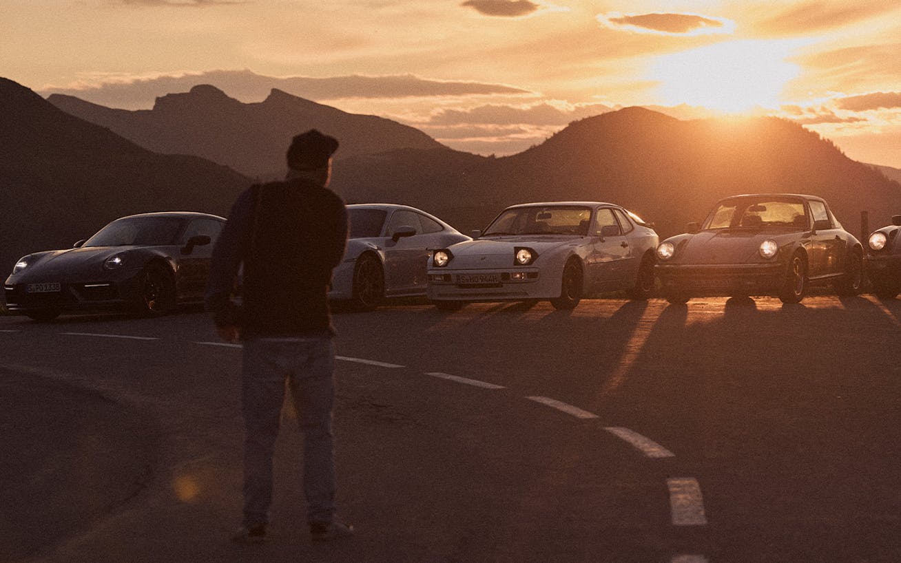 Man photographs line-up of Porsche sportscars at sunset in mountains