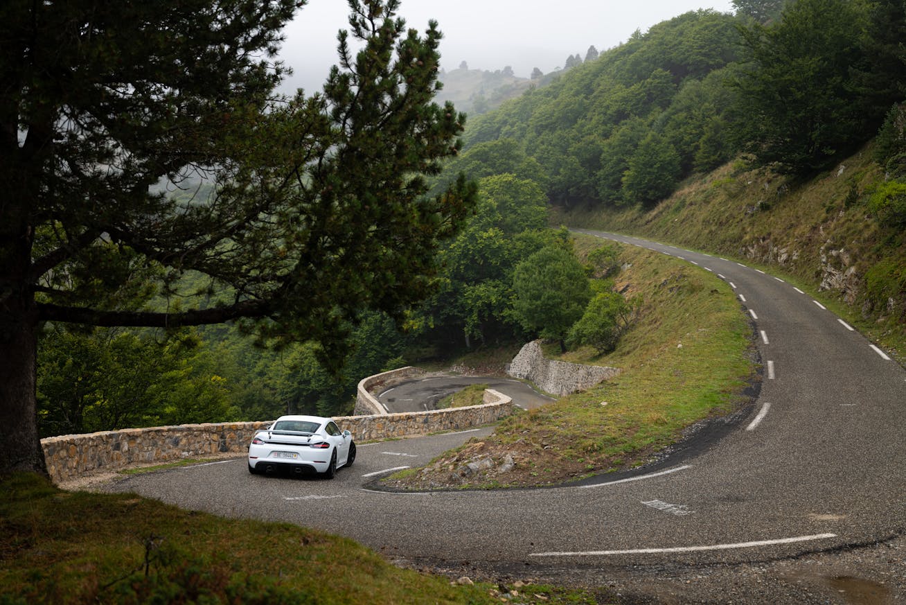White Porsche 718 Cayman GT4 on twisting, tree-lined road