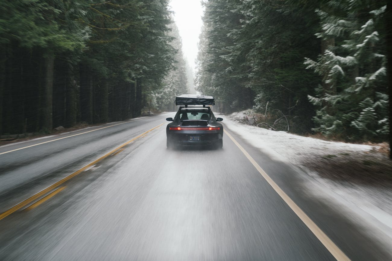 Porsche 911 driving on a snowy road, cutting through forest