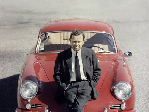 Ferry Porsche is leaning against the front of a red Porsche 356 “No 1” Roadster.
