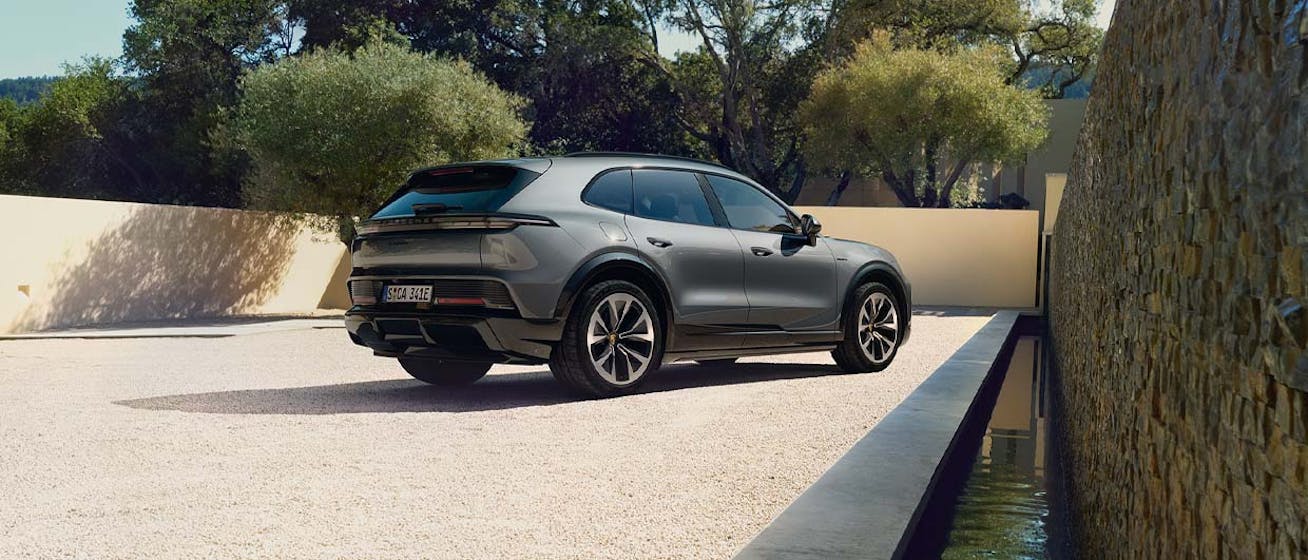 Rear three-quarter view of Porsche Cayenne Electric in modern courtyard surrounded by trees