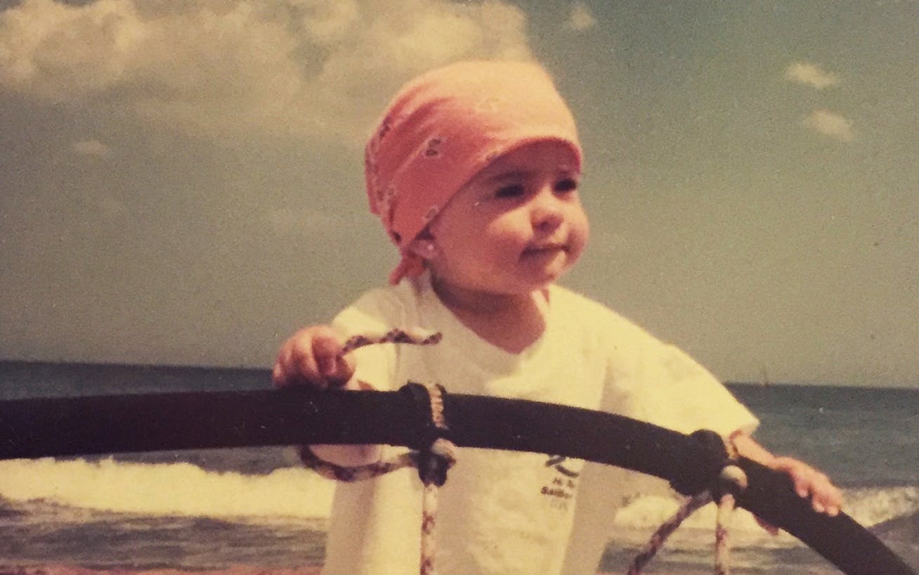 Small child on beach holding on to windsurfing equipment