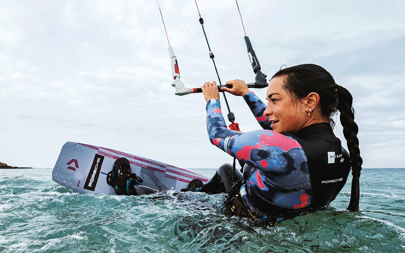 Female kitesurfer in the ocean, holding on to kitesurfing sail