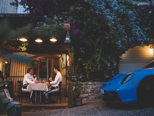Two men at restaurant table beside blue Porsche 911 GT3