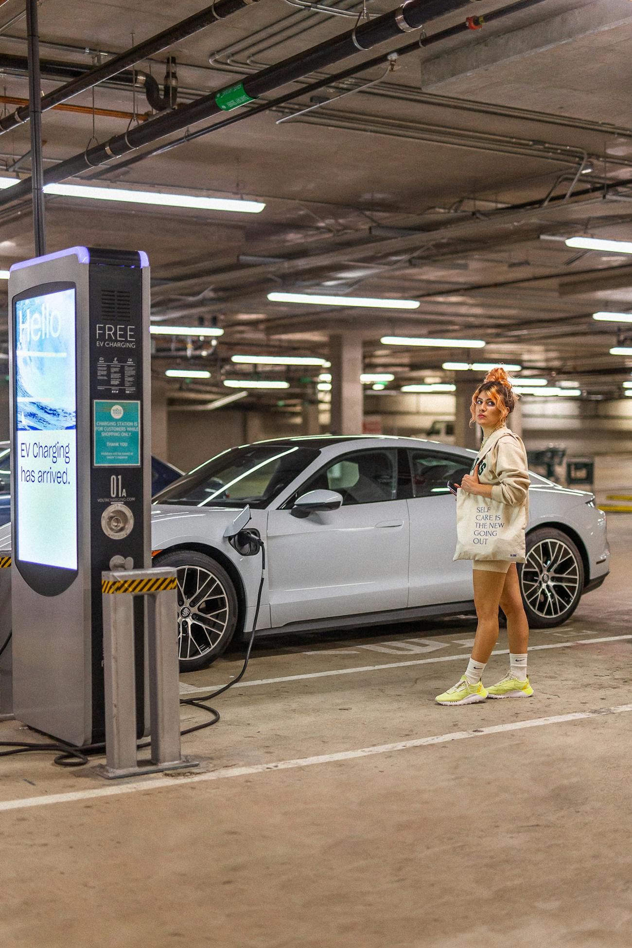 Woman standing by white Porsche Taycan at charging point
