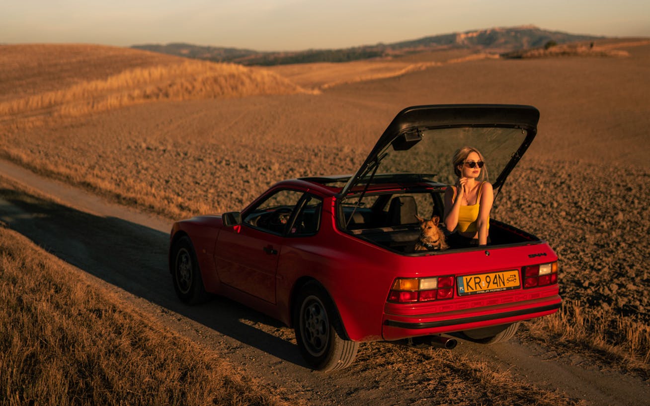 Young woman and dog in back of red Porsche 944 