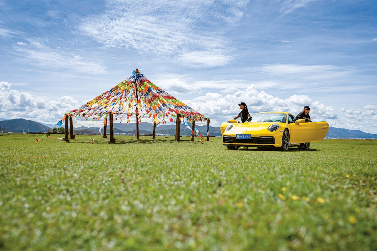 Yellow Porsche 911 Carrera in front of display of prayer flags on Tibetan plateau