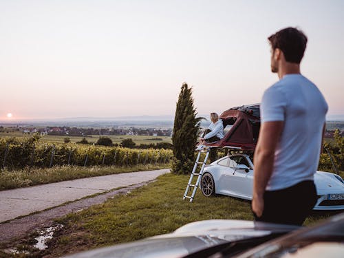 Man in foreground, woman in car roof tent in countryside