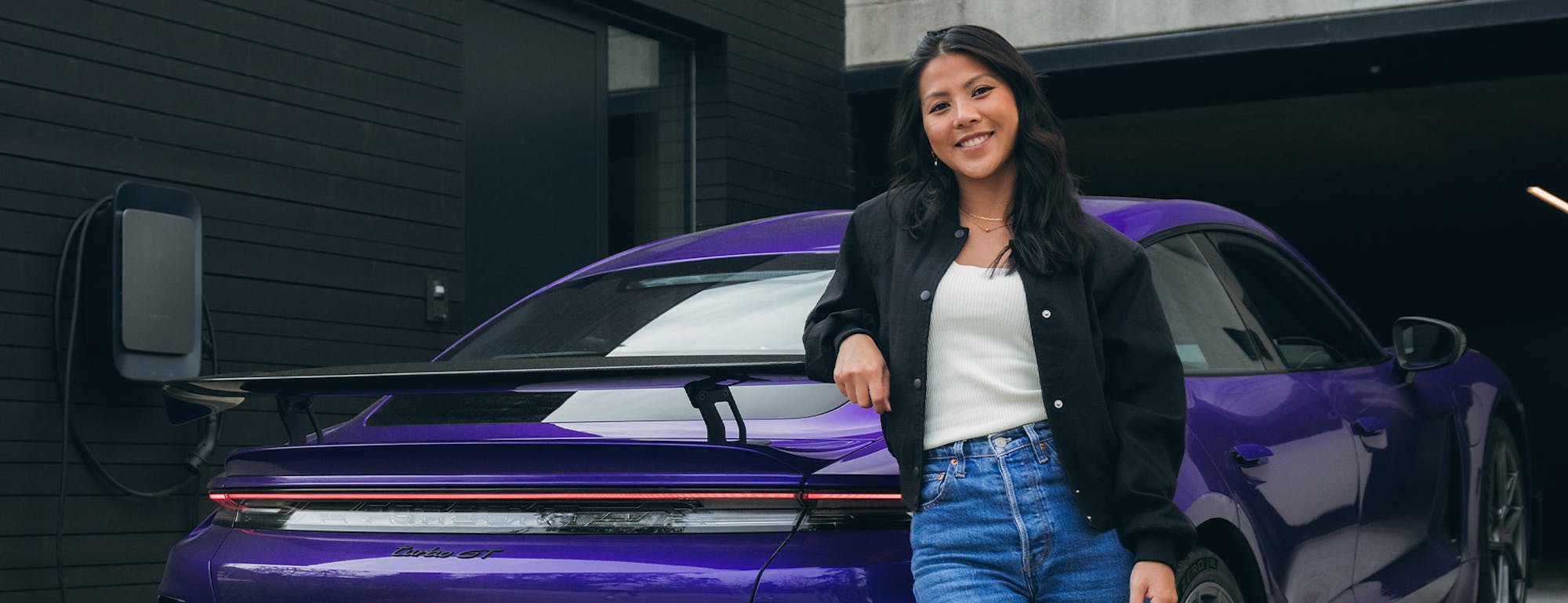 Smiling woman posing with purple Taycan Turbo GT in driveway