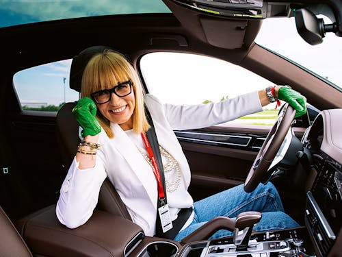 Woman in blazer and green gloves at wheel of Porsche
