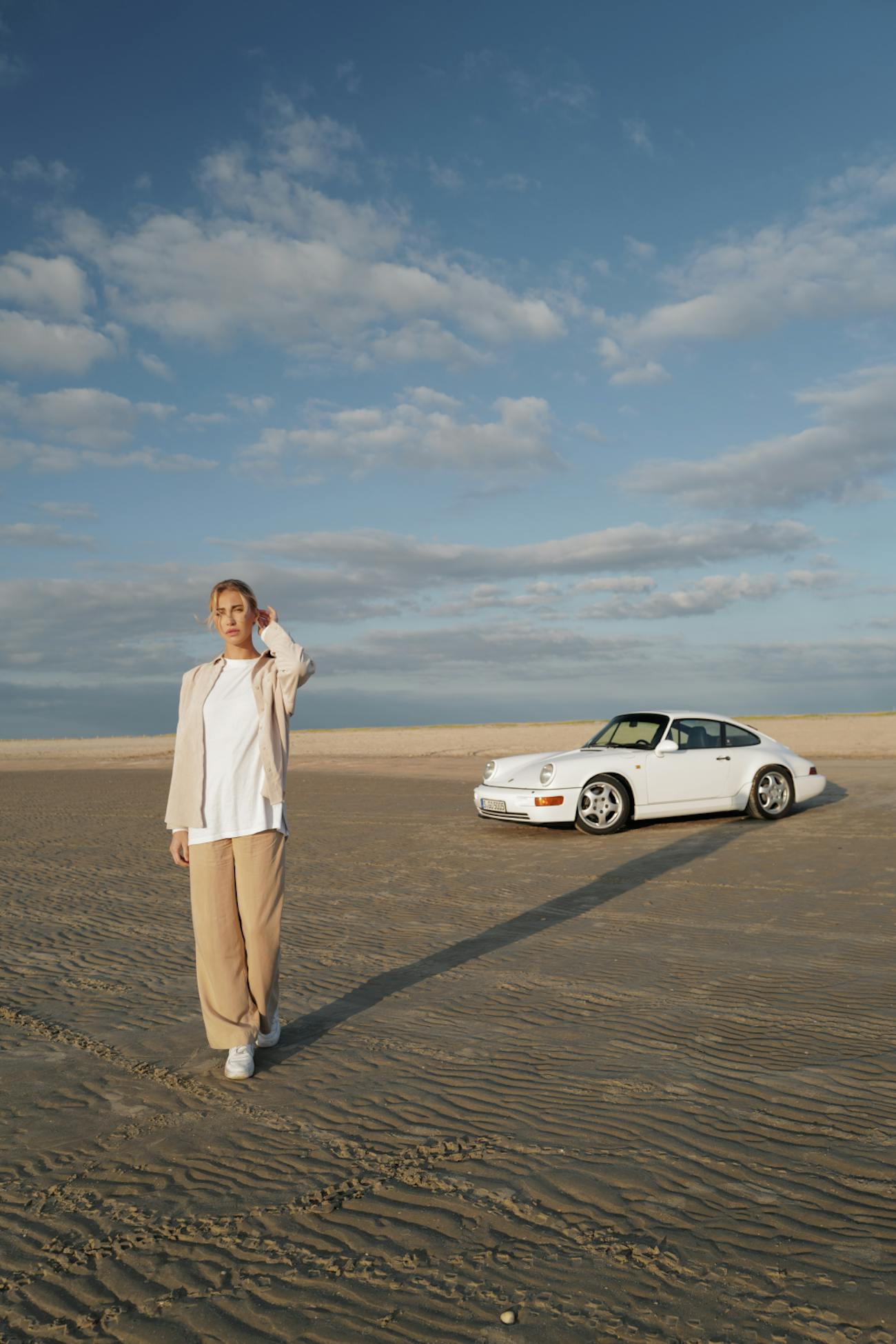 Woman standing on beach, white Porsche 964 in background