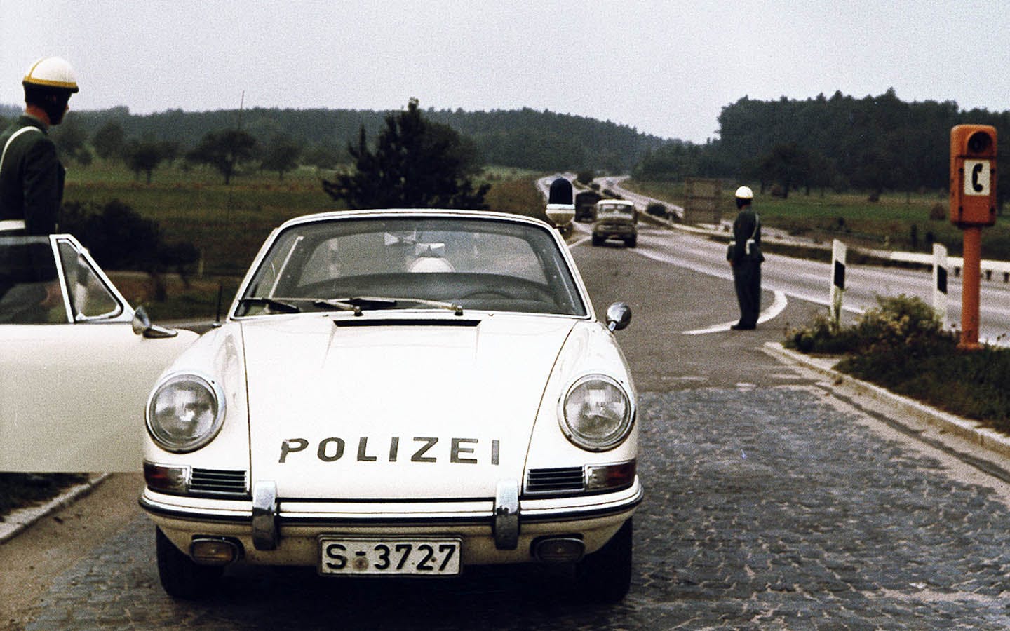 Front view of Porsche 911 police car with helicopter flying overhead