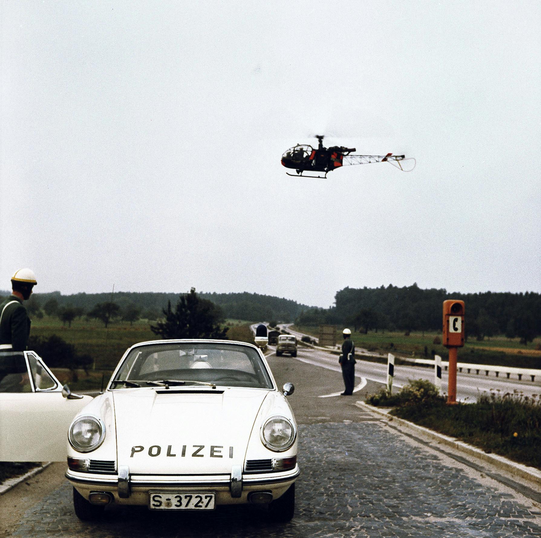 Front view of Porsche 911 police car with helicopter flying overhead