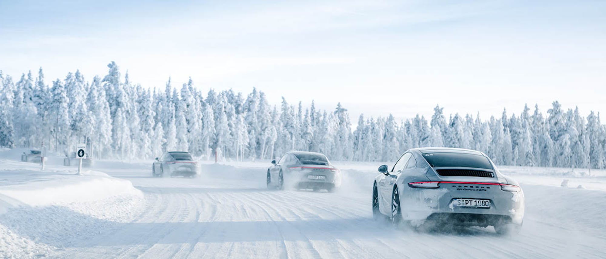 5 grey Porsche 911 Carrera 4 GTS driving on snow in snowy landscape
