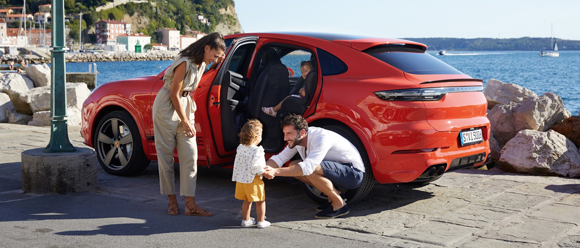 Man, woman and child next to orange Cayenne on seafront