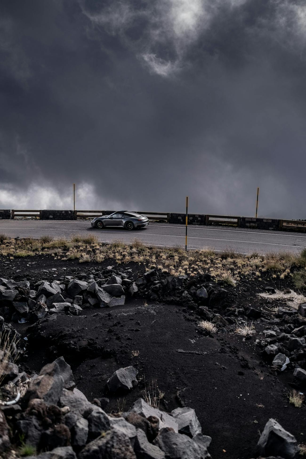Porsche 911 Targa on road surrounded by dark, volcanic rocks