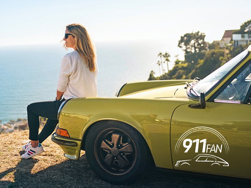 Woman sat on hood of green Porsche 911 overlooking ocean