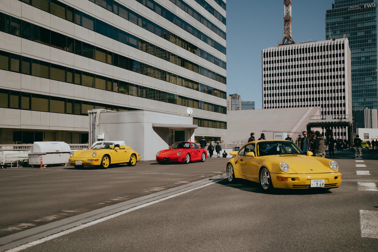 A yellow Porsche 911 Turbo (type 964), a red Porsche 959 and a yellow Porsche 911 Speedster (type 964) displayed on Tokyo’s KK Line during Luftgekühlt