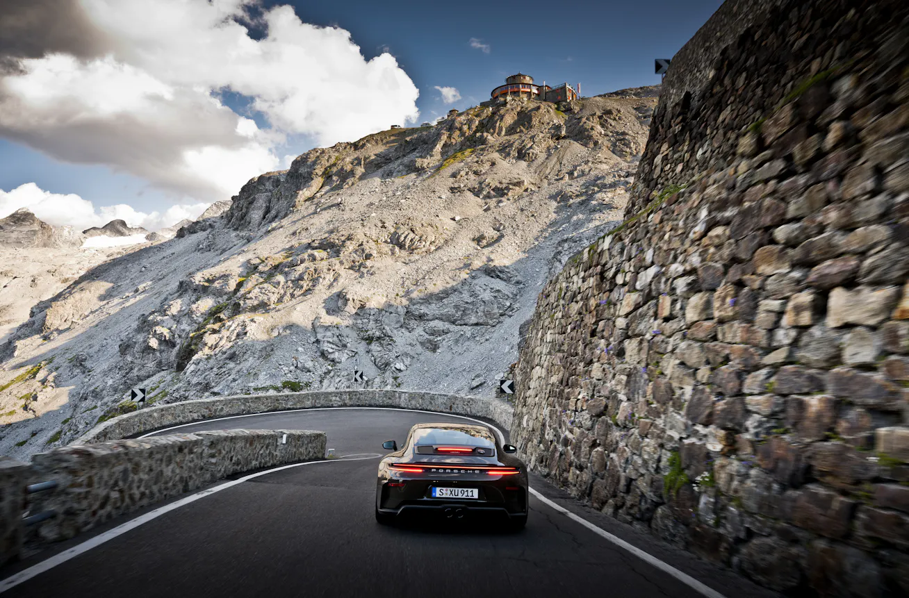 Rear view of GT3 Bergsport driving down Alpine road with mountains in background