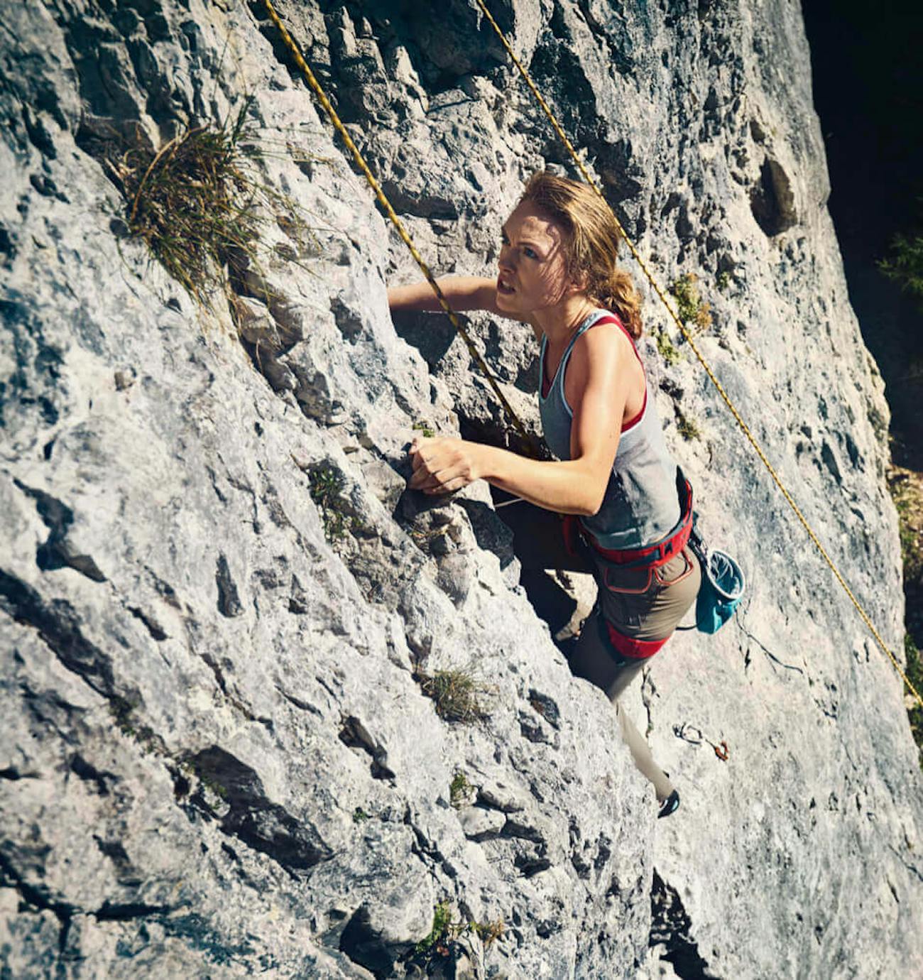 Woman attached to guide ropes climbs up a rock face