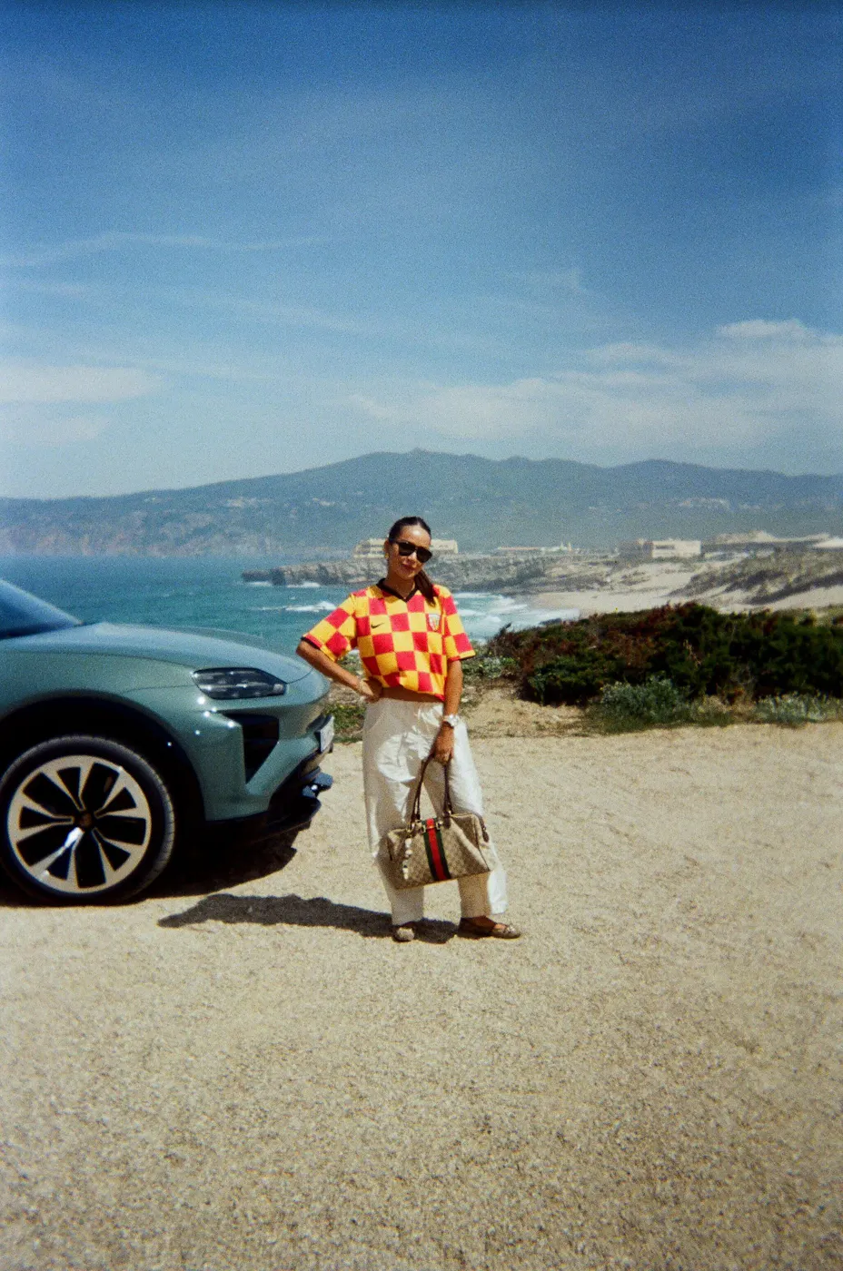Woman standing in front of Porsche Cayenne Electric with coast in background
