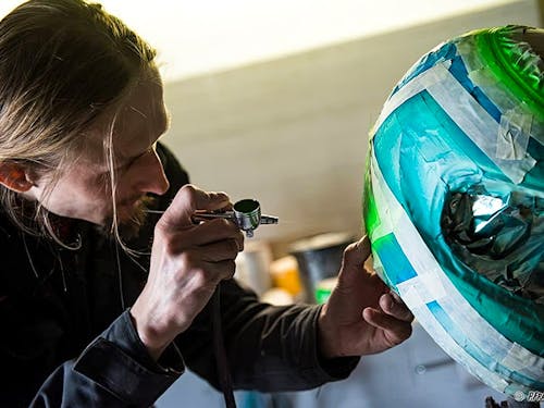 Designer sprays racing helmet with airbrush paint 
