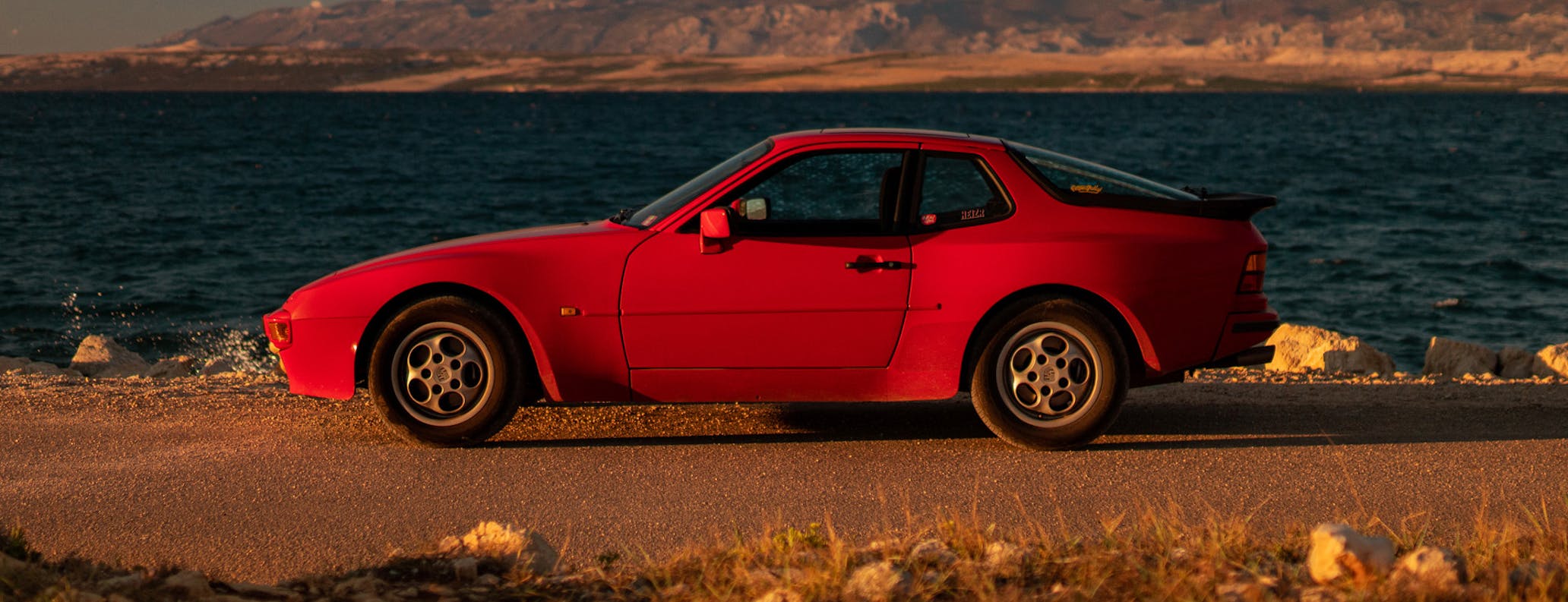 Red Porsche 944 parked by sea at golden hour