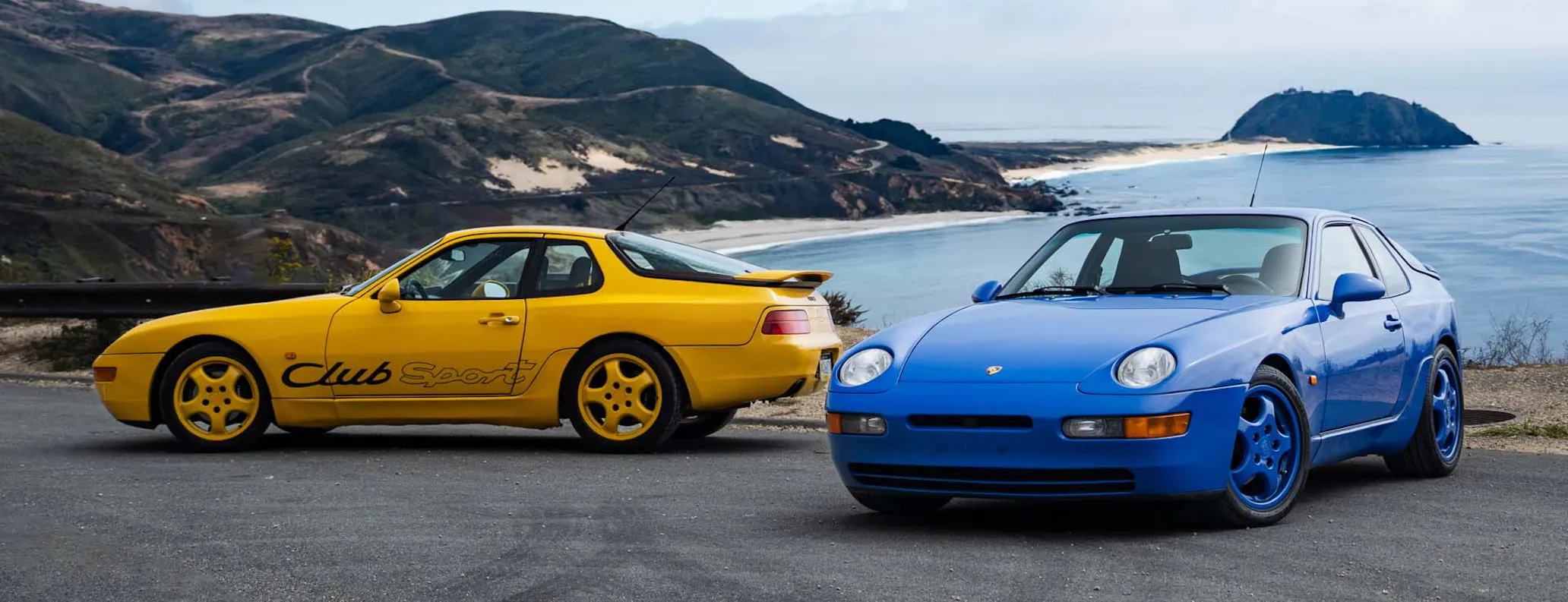 Two Porsche 968 Club Sport cars in Speed Yellow and Maritime Blue with backdrop of Big Sur, California