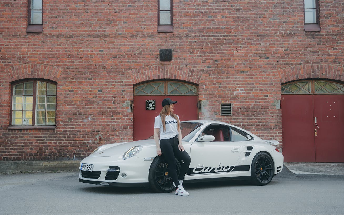 Woman leaning on white Porsche 997 Turbo in parking lot 