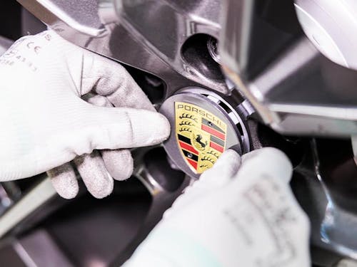 Close-up of hands putting Porsche logo on hub of wheel