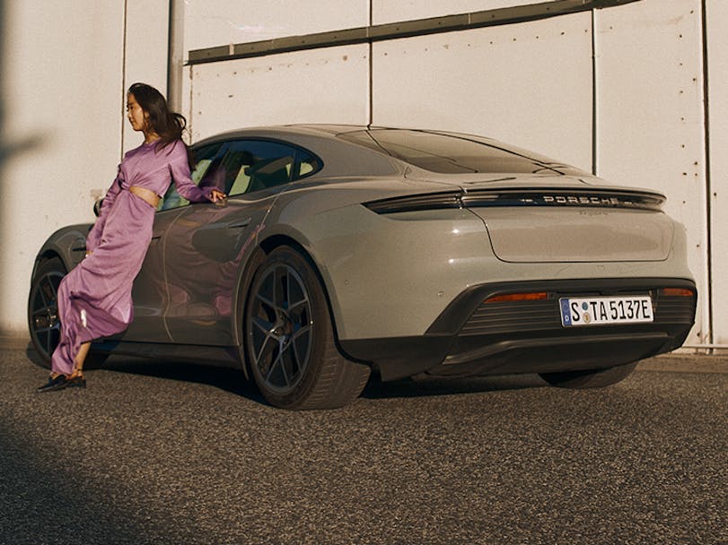 Woman in pink dress leaning up against Porsche Taycan