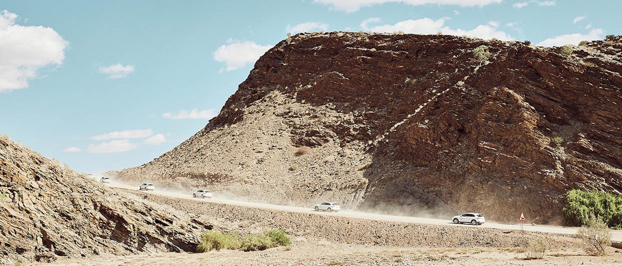 Cars driving on rough terrain in front of a mountain
