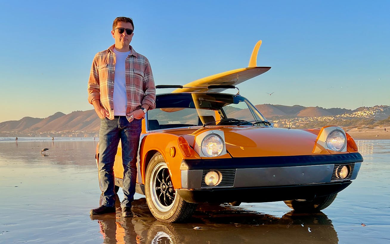 Man standing next to Signal Orange Porsche 914 on beach