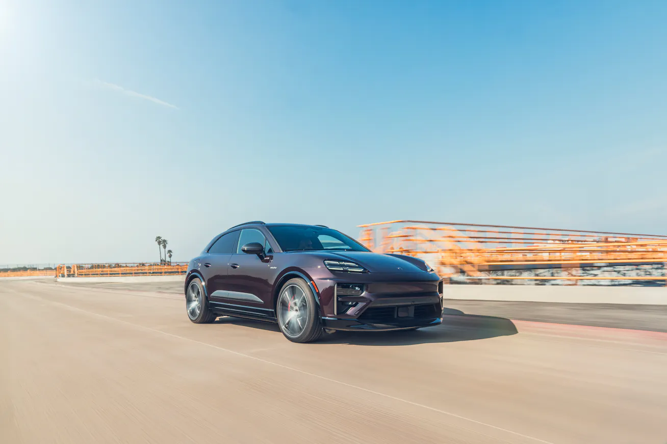 Porsche Macan Electric driving on wide road with modern building in the background