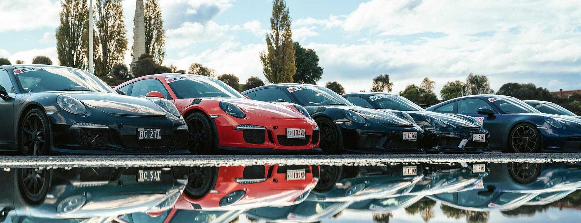Five Porsche cars in a line reflected in water