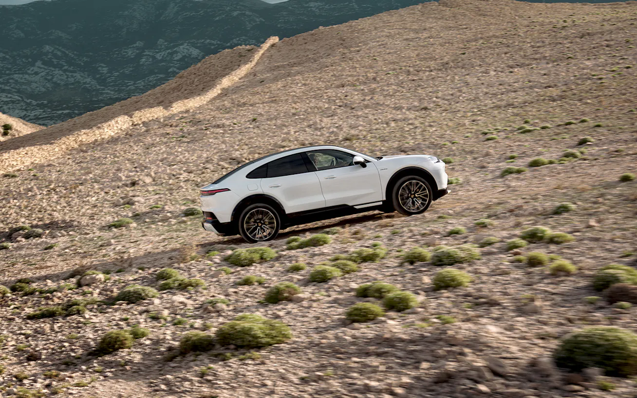 Side view of Cayenne S Coupé Electric driving up incline on a gravel road