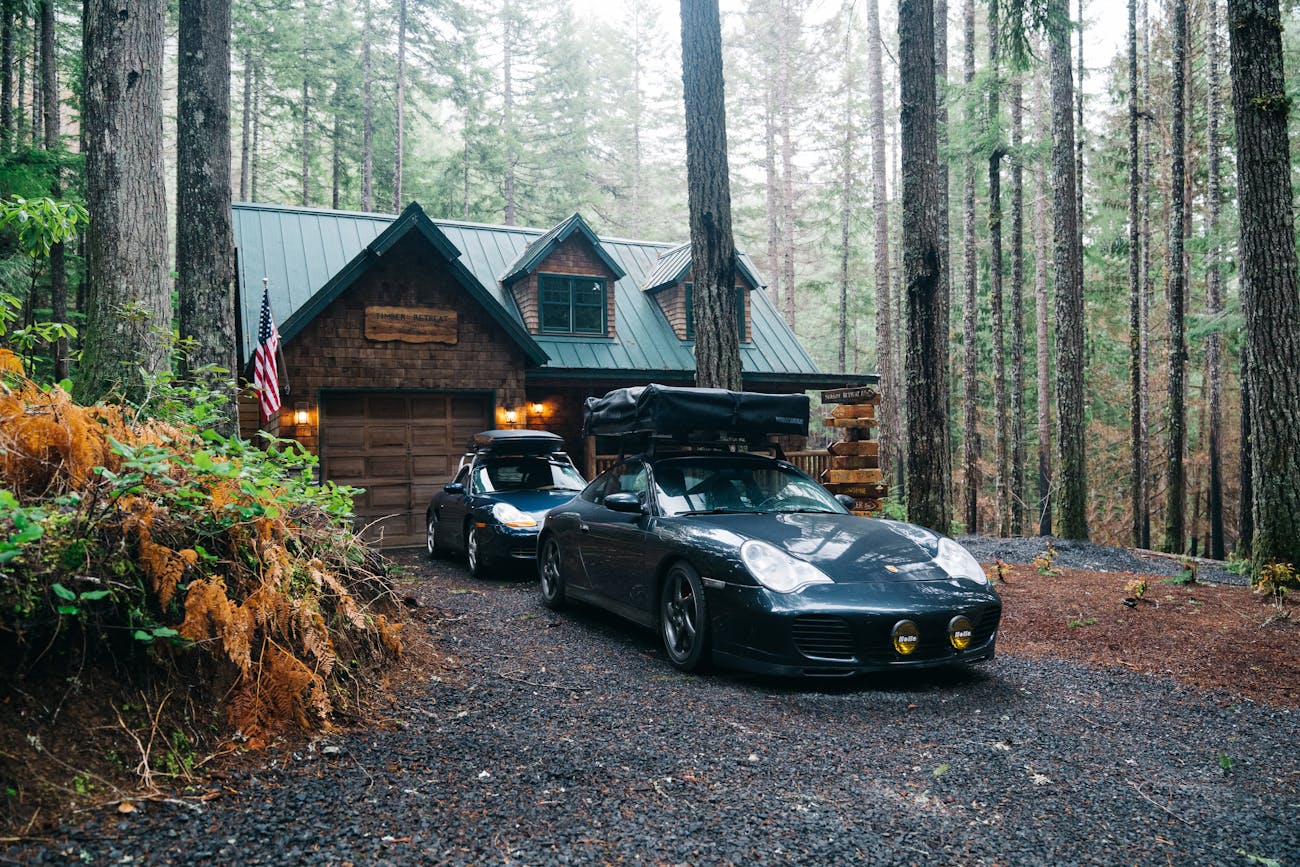 Two Porsche cars parked up outside cabin in the woods