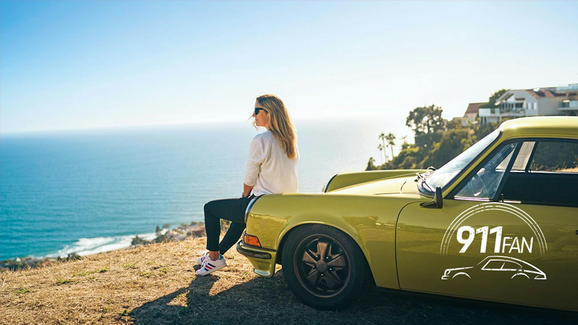 Woman sat on hood of green Porsche 911 overlooking ocean