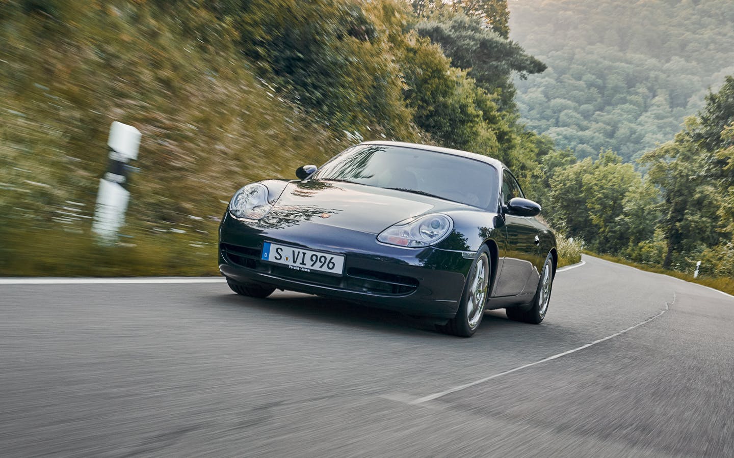 Porsche 911 (type 996) featuring the famous ‘fried egg’ headlights on a hilly road, surrounded by woodland