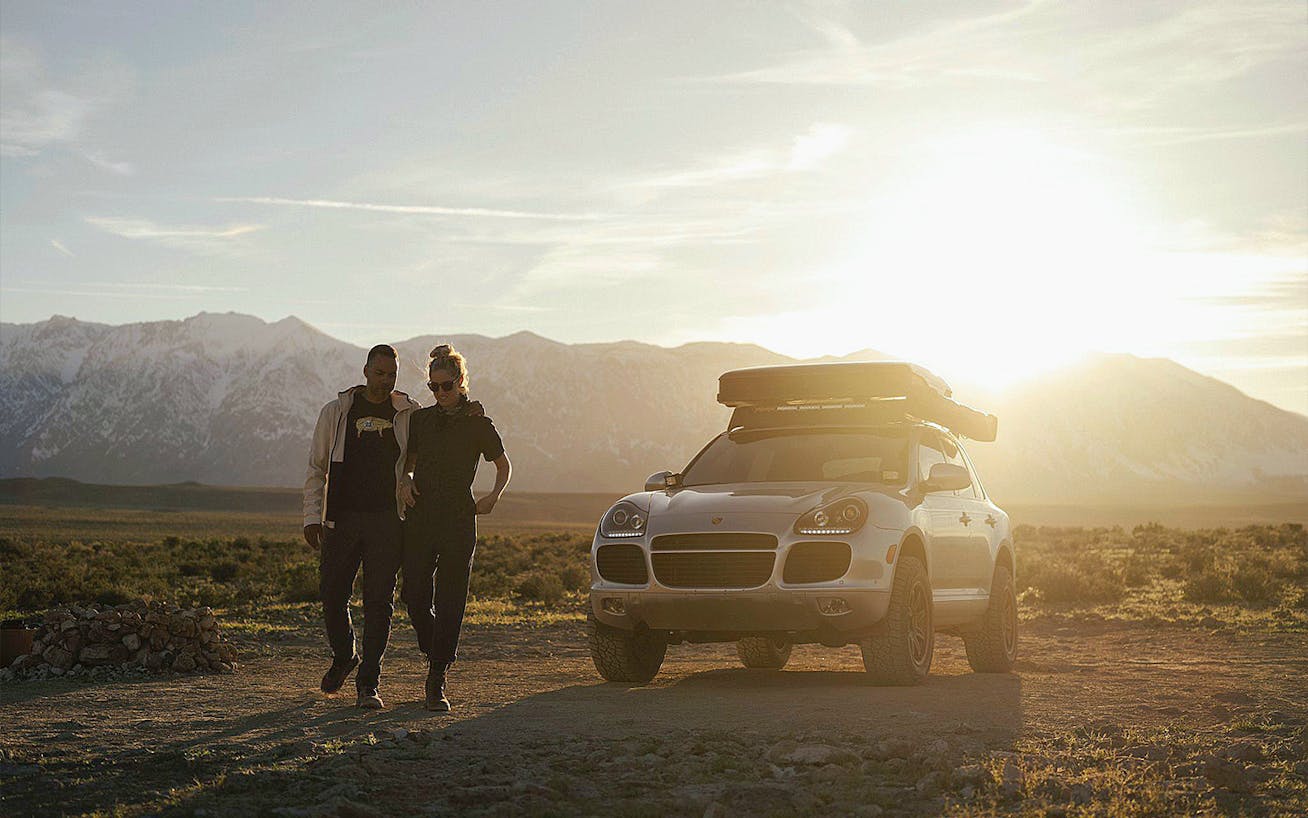 Couple walking away from Porsche Cayenne Turbo at sunset 