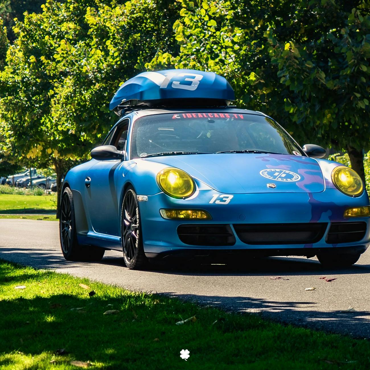 Blue Porsche 911 with roofbox drives along tree-lined road