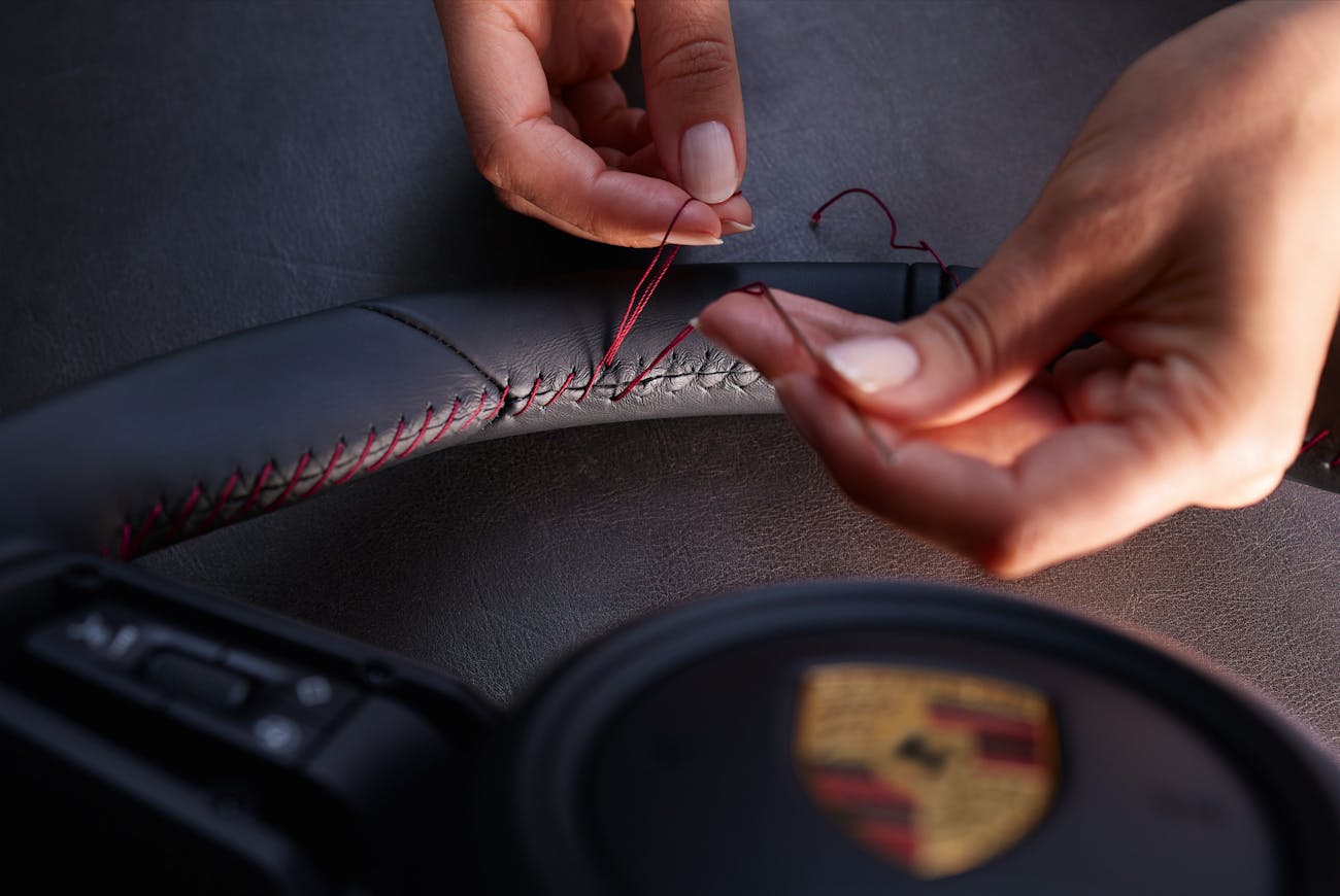 Hands holding unfinished red stitching on a Porsche steering wheel